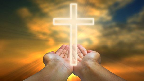 Руки, держащие христианский крест на голубом небе с белыми облаками и солнцем - Фото, изображение