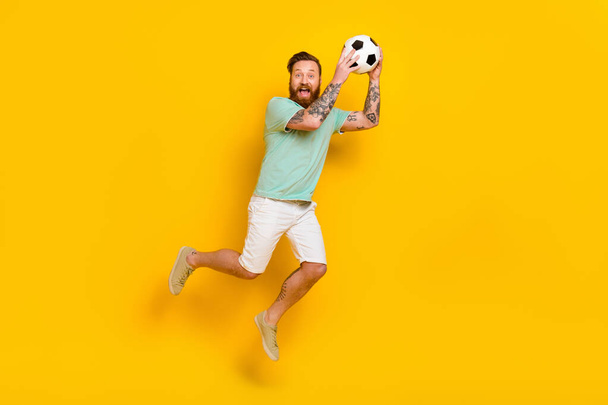 Full length body photo of young overjoyed energetic professional football player guy sporty catch sphere isolated on yellow color background. - Fotoğraf, Görsel