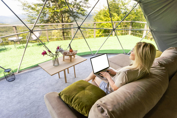 Nuori valkoihoinen nainen, joka käyttää ja katselee kannettavaa tietokonetta telttailuhotellissa. Matkailu, loma ja viikonloppu - Valokuva, kuva