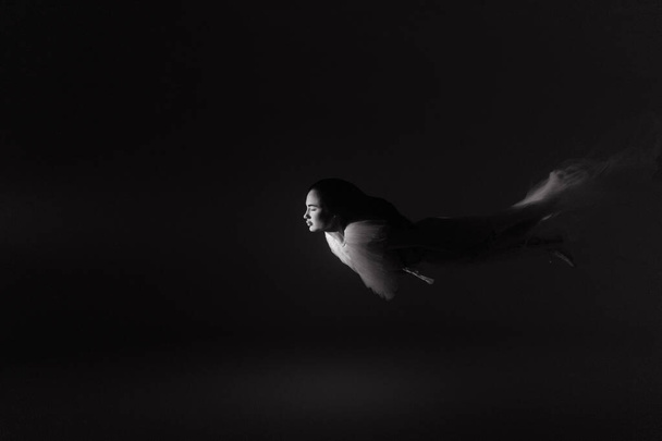 Unterwasser-Shooting der schönen Frau in weißem fliegendem transparentem Kleid, die im beleuchteten Wasser durch Licht schwimmt. Fantasie-Meerjungfrau vor Wasserhintergrund mit Lichtstrahl. Schwarz-Weiß-Bild. - Foto, Bild