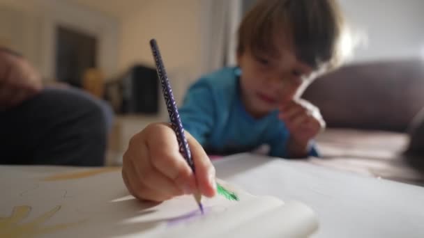 Egy kisfiú, aki papírra firkál színes ceruzával. Közelíts rá a gyerek kézfestésére a füzetben. Gyermekkori fejlesztési tevékenység - Felvétel, videó