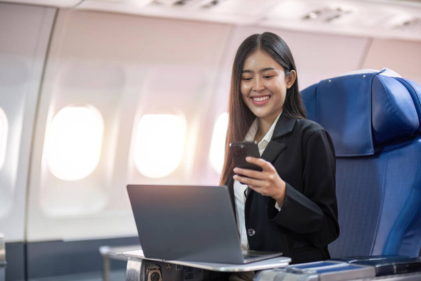 Viajes y tecnología. Volando en primera clase. Mujer de negocios bastante joven usando teléfono inteligente mientras está sentado en el avión. - Foto, Imagen