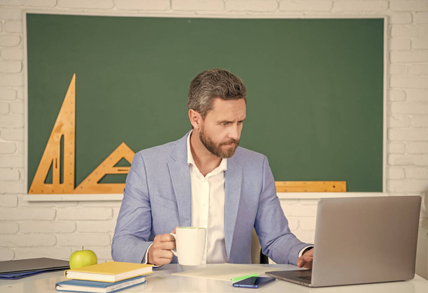 busy school tutor in classroom with laptop having coffee break. - Foto, Imagen