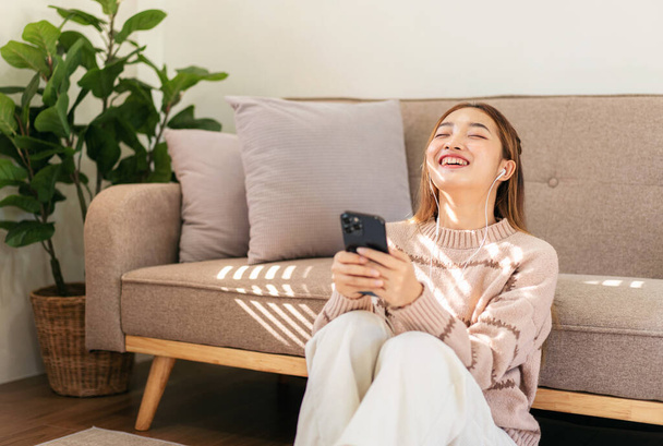 Woman enjoying dreamy and relaxing with listening the music while sitting on the floor to wearing earphones and holding smartphone to leisure with cozy lifestyle in living room at home. - Fotó, kép