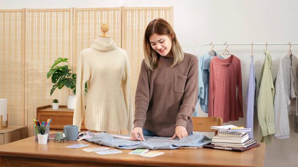 Kadın tasarımcı, ev atölyesinde yeni bir koleksiyon tasarlarken gömlek boyutunu ölçmek ve ayrıntıları kontrol etmek için mezura kullanıyor. - Fotoğraf, Görsel