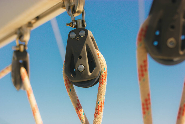 Ship block with ropes. Steel sling and rope clamp connected by screw bolt. Device for adjusting the tension or length of ropes on the deck of a ship, yacht. Boat parts. Roller blocks against blue sky. - Fotó, kép