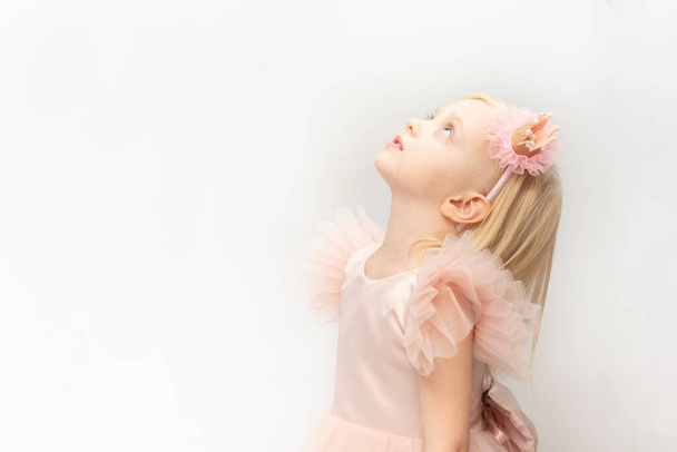 Blonde princess in pink dress and elegant hoop looks up. Little girl isolated on white background. Copy space. - Foto, Imagem