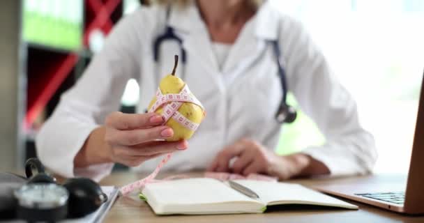 Arzt bietet Birnenobst und Nahrungsmittel mit Vitaminen für die Ernährung an. Ernährungswissenschaftlerin zeigt reife gelbe Birne mit Maßband - Filmmaterial, Video