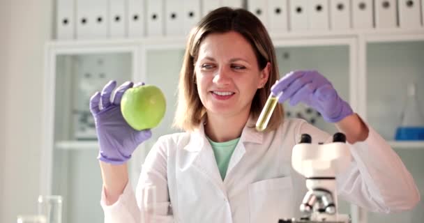 Biologo scienziato tiene tra le mani una mela fresca e tubo con campione di liquido verde. Studio della frutta OGM e tossine - Filmati, video