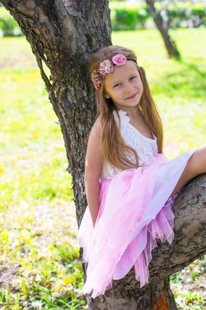 Little adorable girl sitting on blossoming tree in apple garden - Foto, Imagen