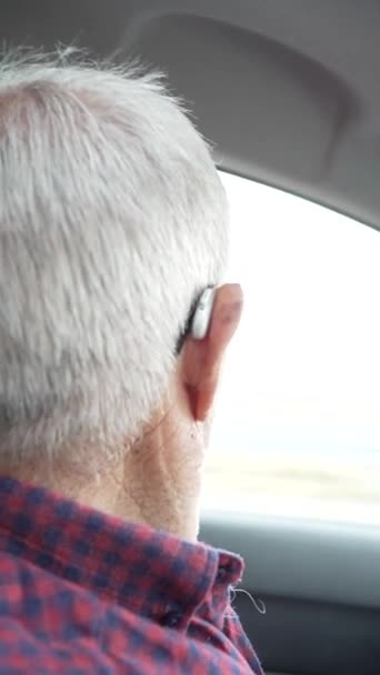 Video des Rentners in seinen Achtzigern am Steuer, Video des Beifahrers zum Fahrer, ernster Mann mit Brille und Kopfhörer, ernster Mann, der die Straße beobachtet - Filmmaterial, Video