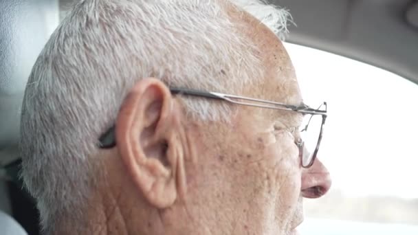 vídeo de anciano jubilado en sus ochenta conducción, vídeo de copiloto a conductor, hombre serio con gafas y auriculares, hombre serio mirando la carretera - Metraje, vídeo