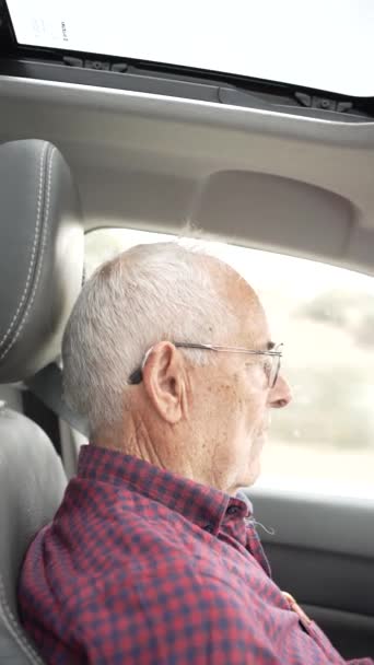 Video eines älteren Rentners über achtzig am Steuer, Video vom Beifahrer zum Fahrer, ernster Mann mit Brille und Hörgerät, ernster Mann, der die Straße beobachtet - Filmmaterial, Video