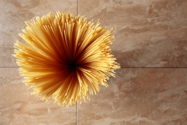 Żółte długie spaghetti na brązowym ceramicznym tle. Żółty włoski makaron. Surowe spaghetti bolognese. Włoskie jedzenie i menu. Widok z góry z miejsca kopiowania.  - Zdjęcie, obraz