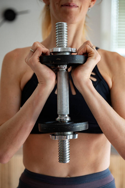 Front view of a fit young woman holding weights in front of her torso. Workout and strength training. - Photo, image