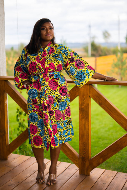 Belle femme afro-américaine profitant d'une soirée sur village et nature sur terrasse de maison de campagne. Diversité et inclusion et chalet - Photo, image