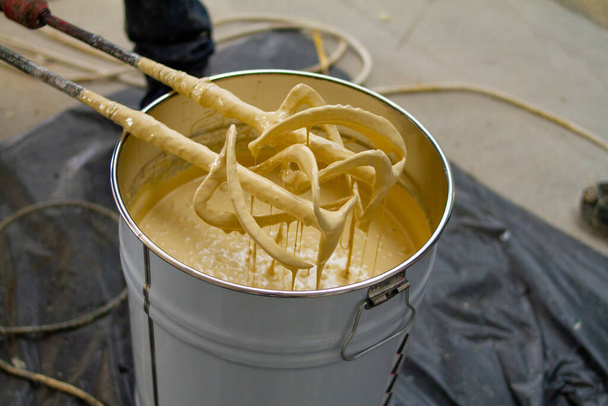 The worker is carefully mixing epoxy composites in a metal bucket to create high-quality polyurethane resin. This process requires precision and attention to detail to ensure the resin is mixed correctly for optimal performance. - Photo, Image