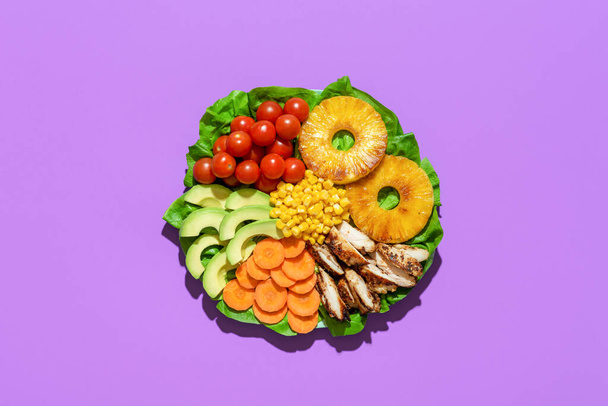 Над видом с гавайским куриным салатом на тарелке, изолированным на фиолетовом фоне. Вкусное летнее блюдо, салат с жареным ананасом и курицей и другими овощами. - Фото, изображение