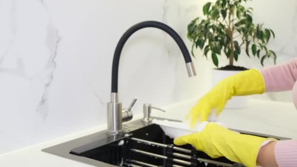 Μια νοικοκυρά πλένει τα πιάτα στο νεροχύτη της κουζίνας χρησιμοποιώντας απορρυπαντικό. Καθαριότητα στο σπίτι - Πλάνα, βίντεο