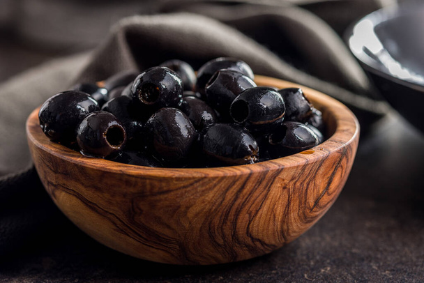 Pitted black olives in wooden bowl on the kitchen table. - Fotografie, Obrázek