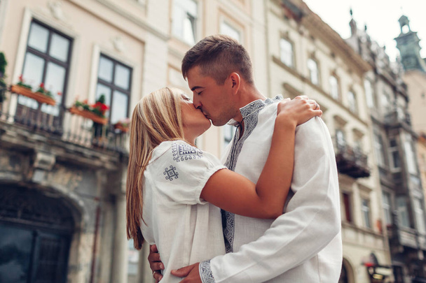 Young couple in love walking in old Lviv city wearing traditional ukrainian shirts. Man and woman hug and kiss outdoors - Photo, image