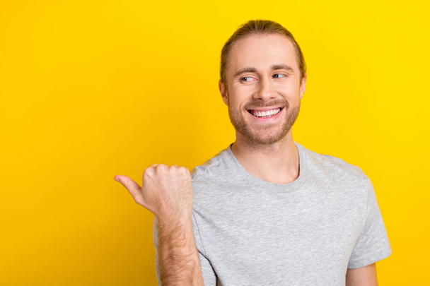 Photo of cheerful satisfied glad man wear trendy grey clothes arm direct empty space nice proposition isolated on yellow color background. - Фото, изображение