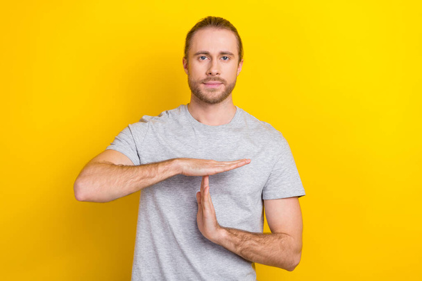 Photo of serious confident guy dressed grey t-shirt showing arms time out isolated yellow color background. - Photo, Image