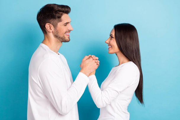 Profile portrait of two idyllic peaceful people hold hands toothy smile look each other isolated on blue color background. - Foto, Bild