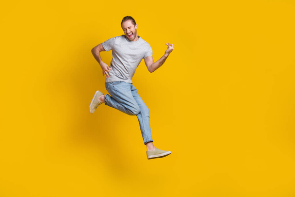 Full length photo of cook cheerful man wear grey t-shirt jumping high playing guitar empty space isolated yellow color background. - Foto, Imagem