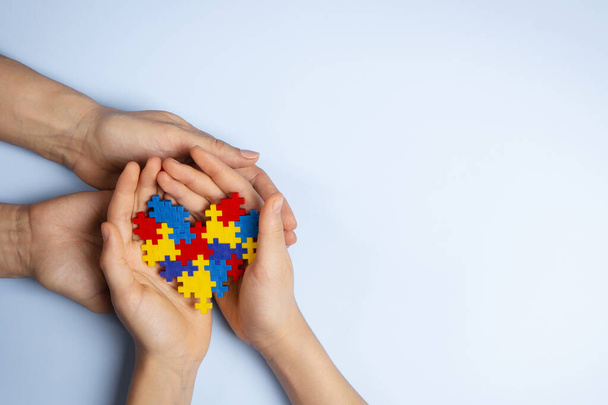 Femme et les mains de l'enfant tenant ensemble le coeur de puzzle coloré sur fond bleu clair. Journée mondiale de sensibilisation à l'autisme, concept de trouble du spectre autistique. - Photo, image