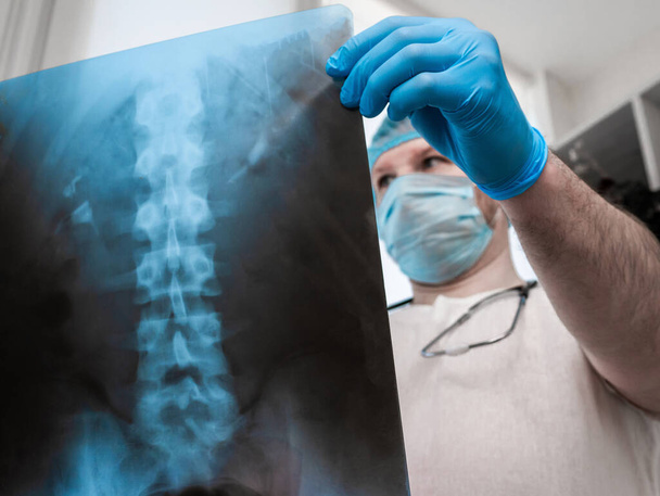Doctor with a stethoscope in the office in the hospital, analyzes the disease of the human spine. Traumatologist vertebrologist with x-ray of the back of the spine of a man. Therapy of osteochondrosis, spinal disease. - Φωτογραφία, εικόνα