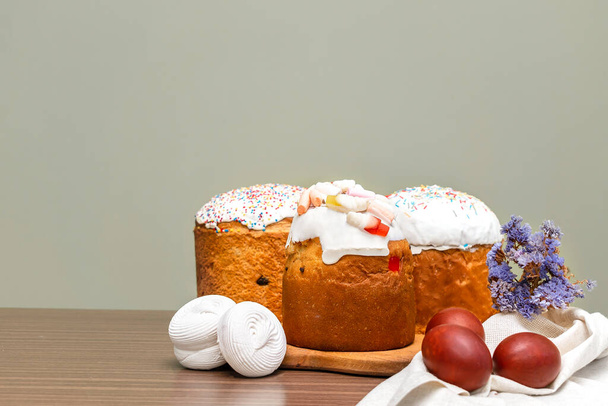 Easter holiday food concept. Homemade Easter cake with white icing, jelly candies, sweet powder, marsmallow, decorated with colored eggs, flowers blossoms on wooden background with copy space. - 写真・画像