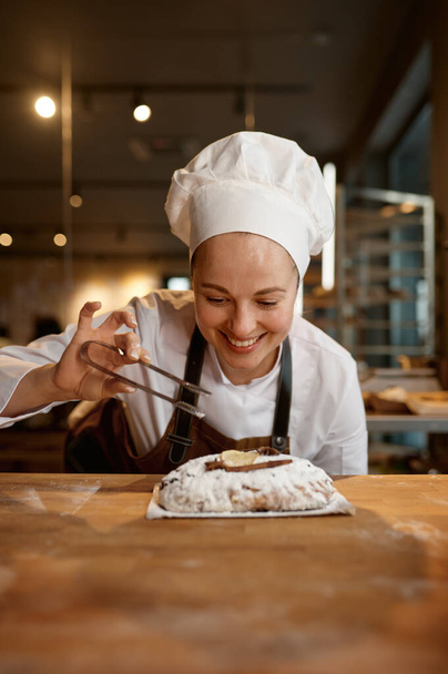 Leipä leipomo työntekijä yllään yhtenäinen ja esiliina koristelu ruokavalio vehnä leipä tai pulla seisoessaan moderni keittiö - Valokuva, kuva