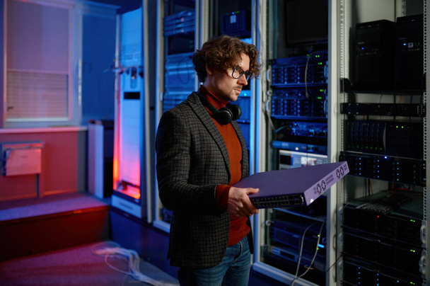 Portrait of it specialist holding hardware component in hand standing in server room. Supercomputer upgrade or repair concept - Фото, зображення