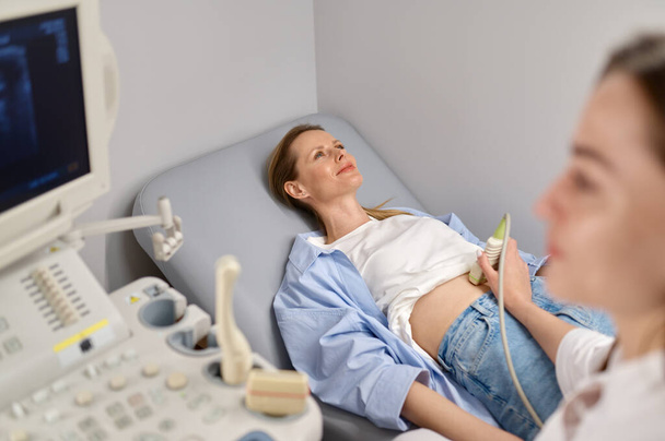 Professzionális orvos vizsgálja meg a betegét hasi ultrahang szkenneléssel ultrahangos szkennerrel. A terhesség korai megerősítésének koncepciója - Fotó, kép