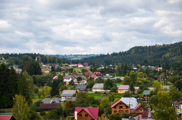 Panorama des grünen Hügellandes mit Häusern und einer bergigen Kulisse im Dorf Worochta, Karpaten, Ukraine - Foto, Bild