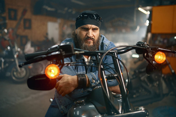 Handsome bearded man testing new motorbike in garage store. Biker choosing new vehicle at motor shop - Photo, Image