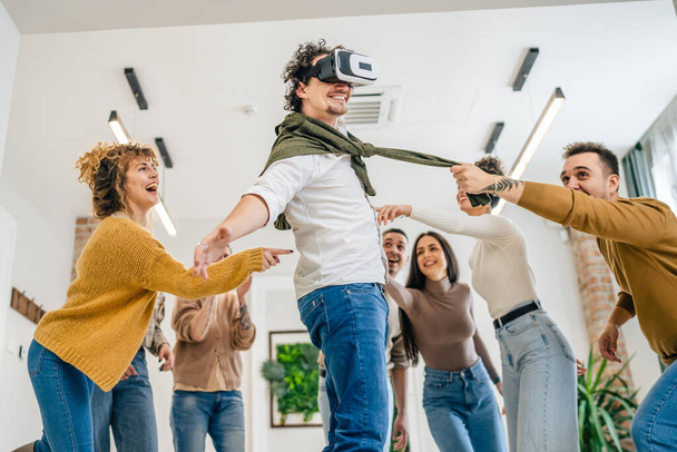 One man adult caucasian male in front of group of men and women friends enjoy virtual reality VR headset at work having fun together during team building seminar real people bright filter - Foto, Bild