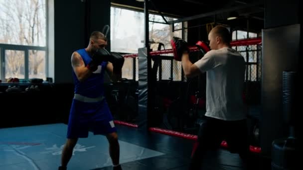 Bokser ćwiczy uderzenia z trenerem w siłowni bokserskiej - Materiał filmowy, wideo