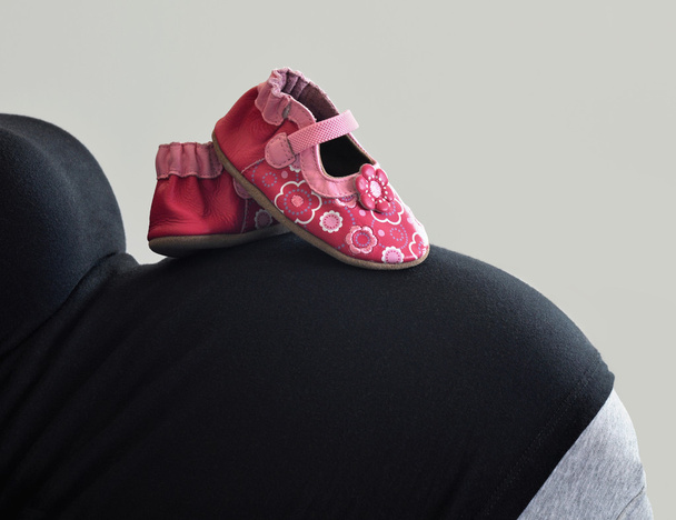 Vaaleanpunaiset kengät tyttövauvalle raskaana olevan äidin vatsaan
 - Valokuva, kuva
