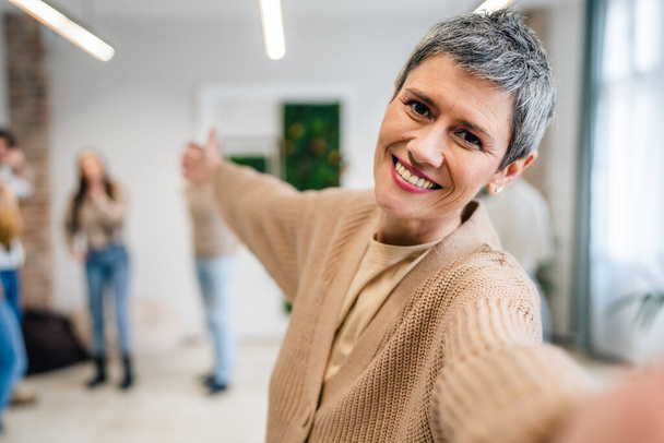 Portrait of senior woman in front of group of people men and women colleagues portrait of caucasian female stand at work happy smile confident with short gray hair copy space bright filter - Fotoğraf, Görsel