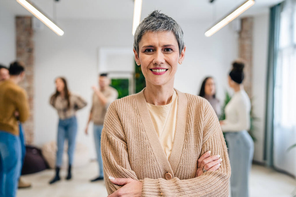 Portrait of senior woman in front of group of people men and women colleagues portrait of caucasian female stand at work happy smile confident with short gray hair copy space bright filter - Foto, imagen