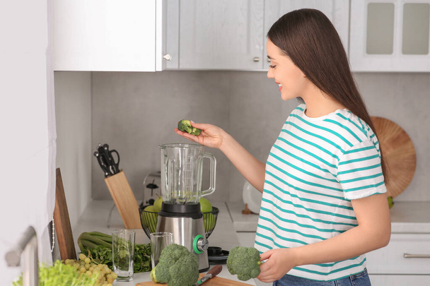 Woman adding broccoli into blender for smoothie in kitchen - Zdjęcie, obraz