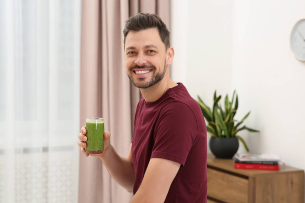 Happy man holding glass of delicious fresh smoothie at home - Foto, Imagem