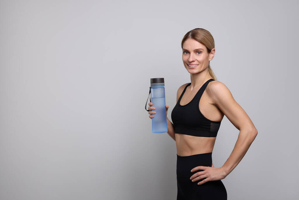 Sportswoman with bottle of water on light grey background, space for text - Foto, imagen