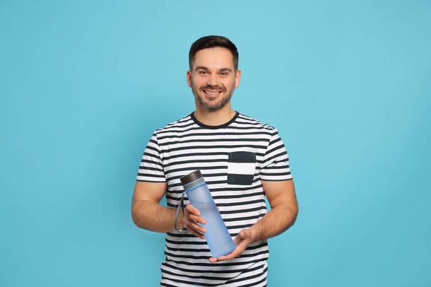 Happy man holding transparent plastic bottle of water on light blue background - Photo, Image