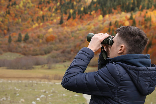 Boy looking through binoculars in beautiful mountains, back view. Space for text - Zdjęcie, obraz