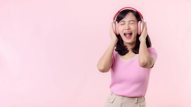 Χαμόγελο όμορφο πρόσωπο μοντέλο ακούσετε μουσική τραγούδι και να απολαύσετε το χορό με ασύρματα ακουστικά σε απευθείας σύνδεση ήχου ραδιόφωνο ήχο. Θετική έξοδος χαρούμενη νεαρή γυναίκα τραγουδά σε ροζ απομονωμένο στούντιο - Φωτογραφία, εικόνα
