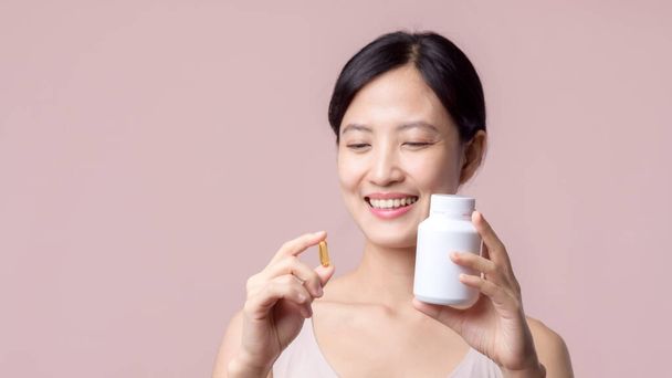 Mladý portrét asijské žena šťastný úsměv tvář s vitamín výživu pilulku. Docela roztomilá dívka žena osoba drží zdravotní kapsle doplněk péče o pleť izolované na růžovém pozadí. Koncept medikace. - Fotografie, Obrázek