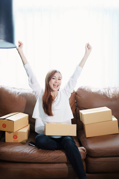 Starting small business entrepreneur of independent Asian woman smiling using computer laptop with cheerful success of online marketing package box items and SME delivery concept. - Foto, Bild